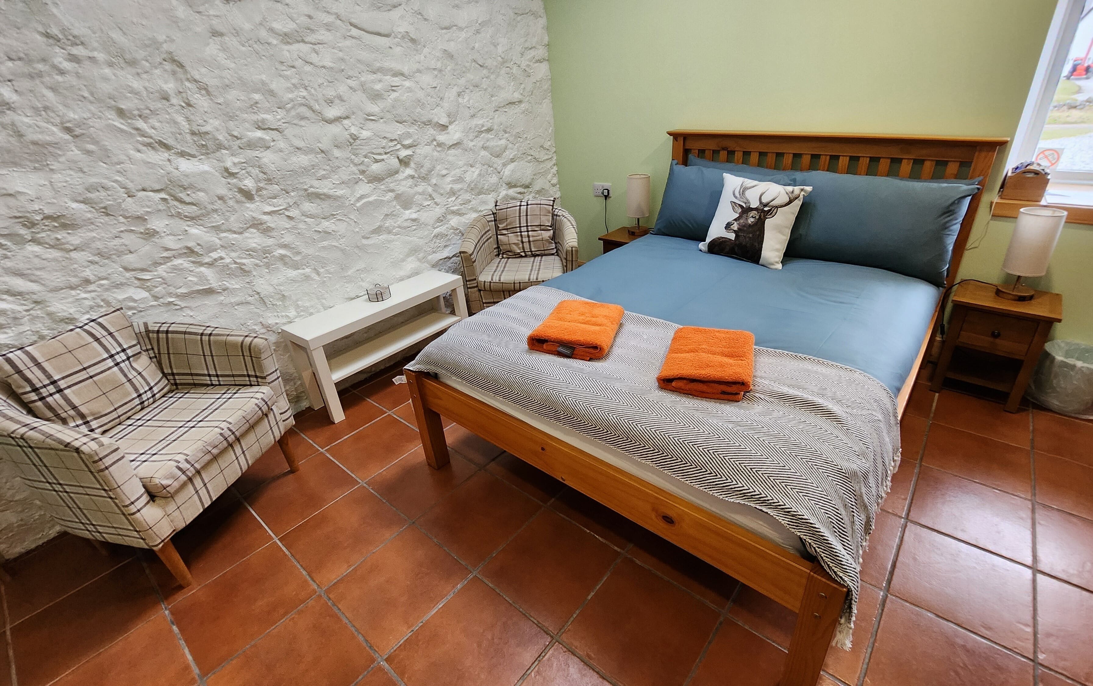 A bedroom with a bed, a chair, a nightstand, and a wall with a textured surface.