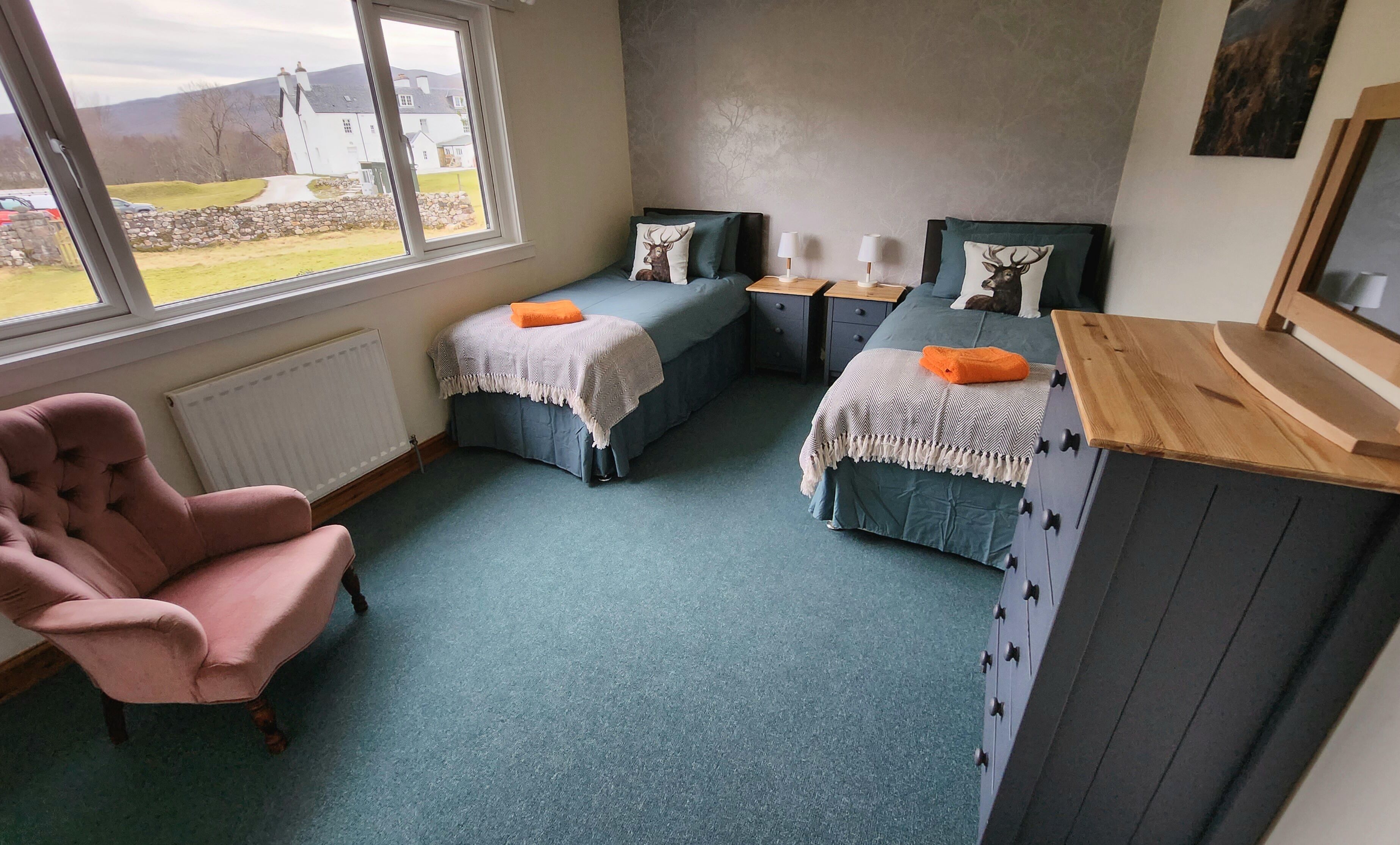 A bedroom with two beds, a chair, and a view of the outside.