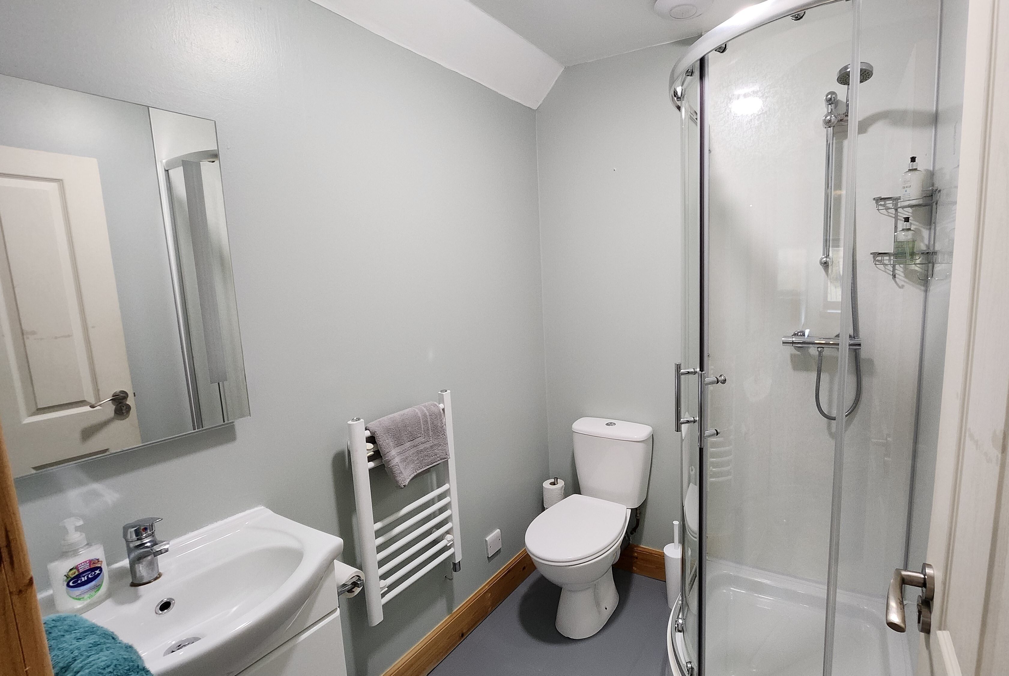 Un baño con lavamanos blanco, inodoro, cabina de ducha de vidrio y espejo.