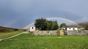 Un paysage rural avec un mur de pierres, une construction en bois et une maison blanche avec un toit de pierres.