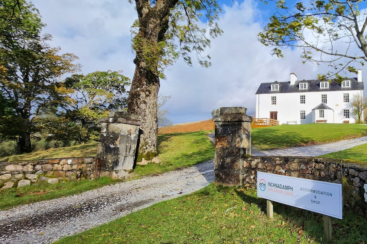 A stone gate leading to a white building with a sign reading "Inchnadamph Accommodation & Shop".