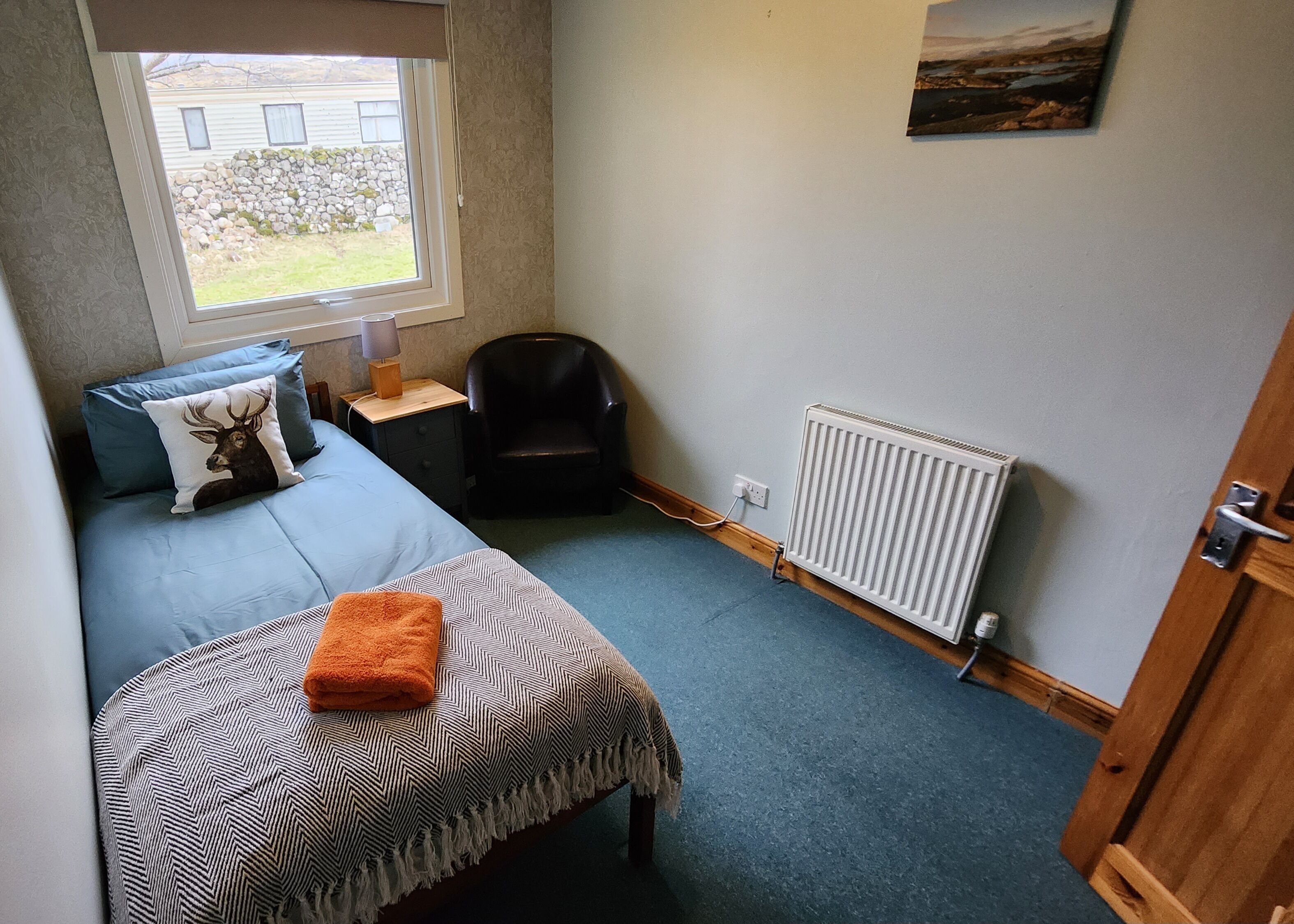 A small, cozy room with a single bed, a chair, a radiator, and a window overlooking a garden.