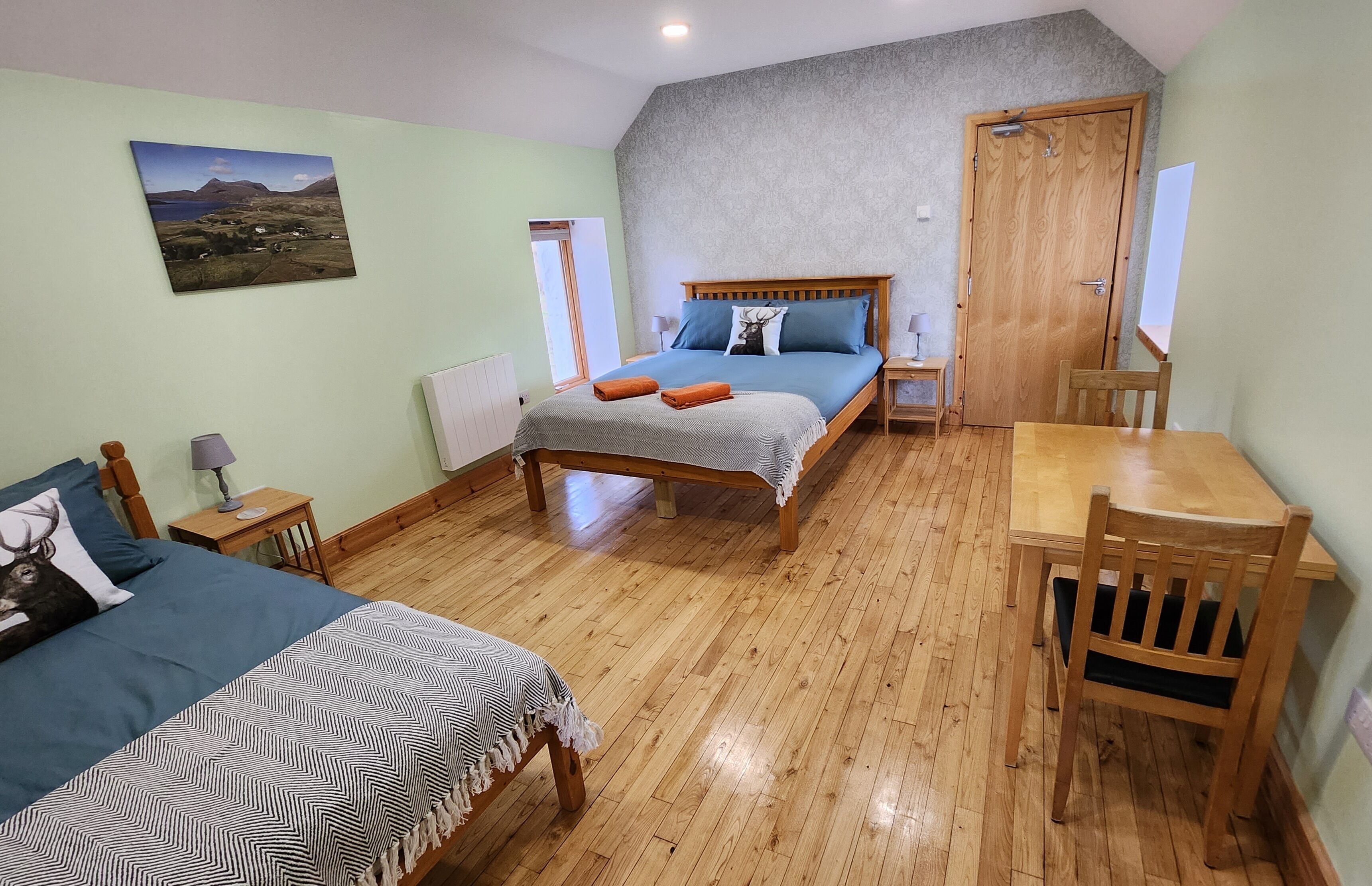 A bedroom with a large bed, a wooden desk, and a chair. There is a window with a view of a landscape.