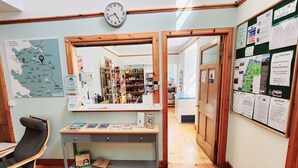 Une pièce avec un bureau en bois, une chaise, une carte accrochée au mur et un miroir qui reflète un couloir avec des étagères et un réfrigérateur.