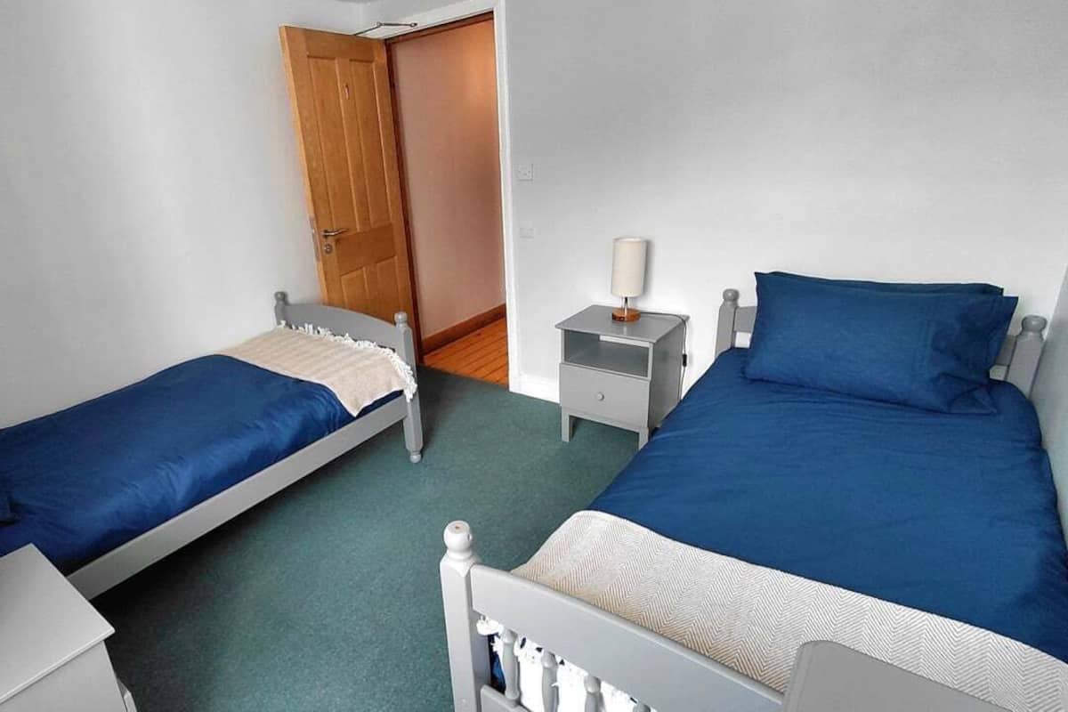 A room with two single beds, a bedside table with a lamp, and a door leading to another room.