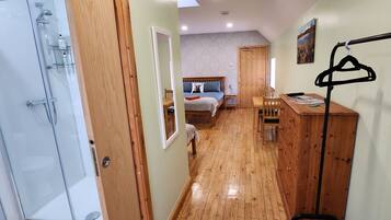 A narrow hallway leading to a bedroom with a bed, a wooden dresser, and a mirror. A shower area is visible on the left.