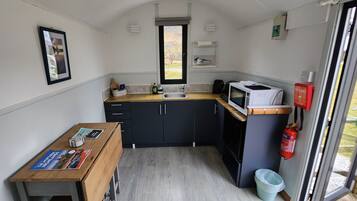 Une cuisine compacte avec des meubles de couleur sombre, un plan de travail en bois, un four à micro-ondes et une petite fenêtre.
