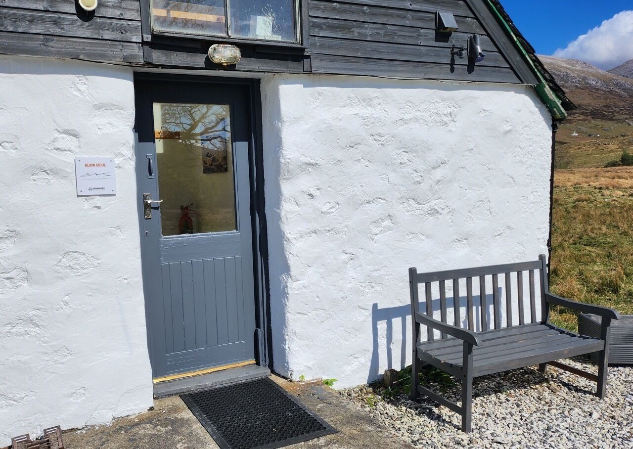 A white building with a grey door and a bench outside.