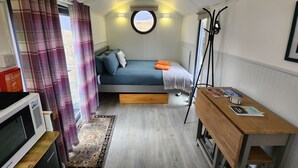 Une chambre à coucher de taille réduite, comprenant un lit, un petit bureau, un four à micro-ondes et une fenêtre avec des rideaux.