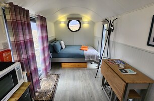 Un dormitorio pequeño con cama, un escritorio, microondas y ventana con cortinas.