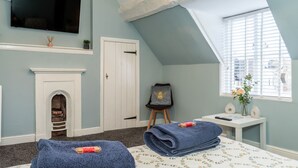 Una habitación con chimenea, una cama con colcha estampada, un televisor montado en la pared y un ventanal con persianas.
