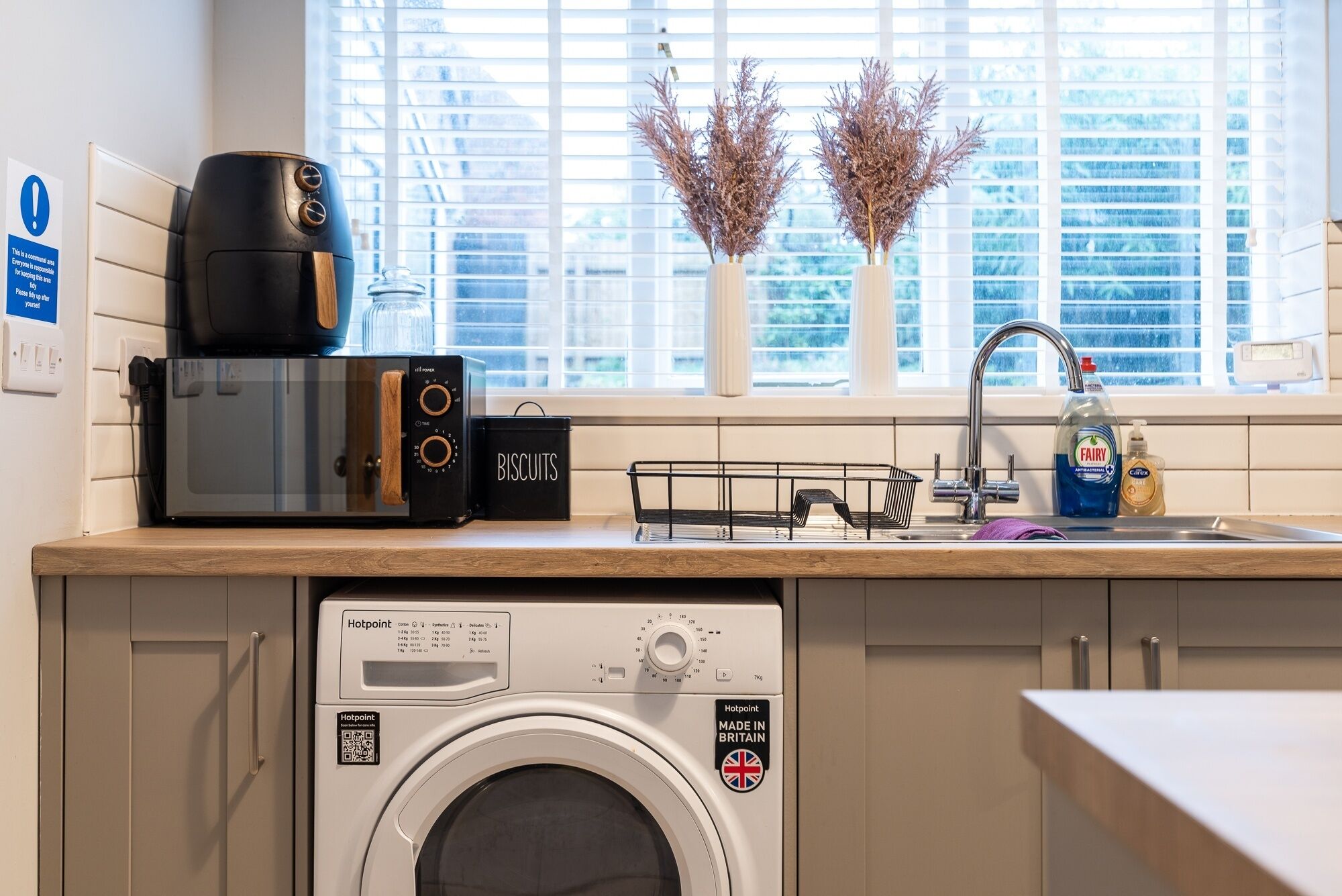A kitchen with a washing machine, a microwave, a toaster, and a sink with a faucet.