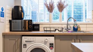 A kitchen with a washing machine, a microwave, a toaster, and a sink with a faucet.