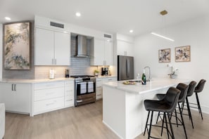 A modern kitchen with white cabinetry, a stainless steel range, and a central island with bar stools.