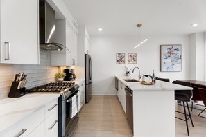A modern kitchen with white cabinetry, a gas stove, a built-in oven, and a stainless steel refrigerator.