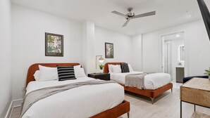 Ein modernes Schlafzimmer mit zwei Betten, einem Deckenventilator und gerahmten Kunstwerken an den Wänden.