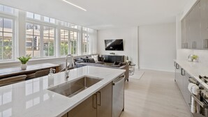Eine moderne Küche mit einer großen Kochinsel, ein Essbereich mit einer Couch und Blick auf Gebäude durch große Fenster.