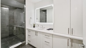 Un baño moderno con cabina de ducha de vidrio, tocador blanco con espejo y lavamanos.