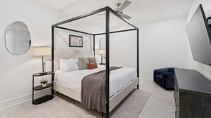 Un dormitorio moderno con cama con dosel, espejo redondo, lámparas de noche y televisor de pantalla plana.