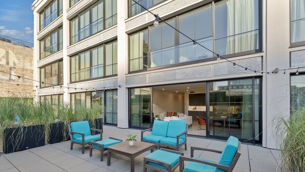 Een modern terras buiten met zitplaatsen en uitzicht op het interieur van het gebouw.