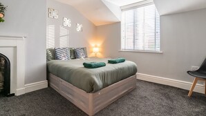 Ein Schlafzimmer mit Bett, Nachttischlampe, einem Fenster mit Jalousien und Deckenleuchte.