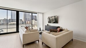 A modern living room with two sofas, a TV on the wall, and a large window with a city view.