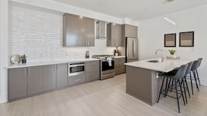 A modern kitchen with stainless steel appliances, a large island with bar stools, and a white brick backsplash.