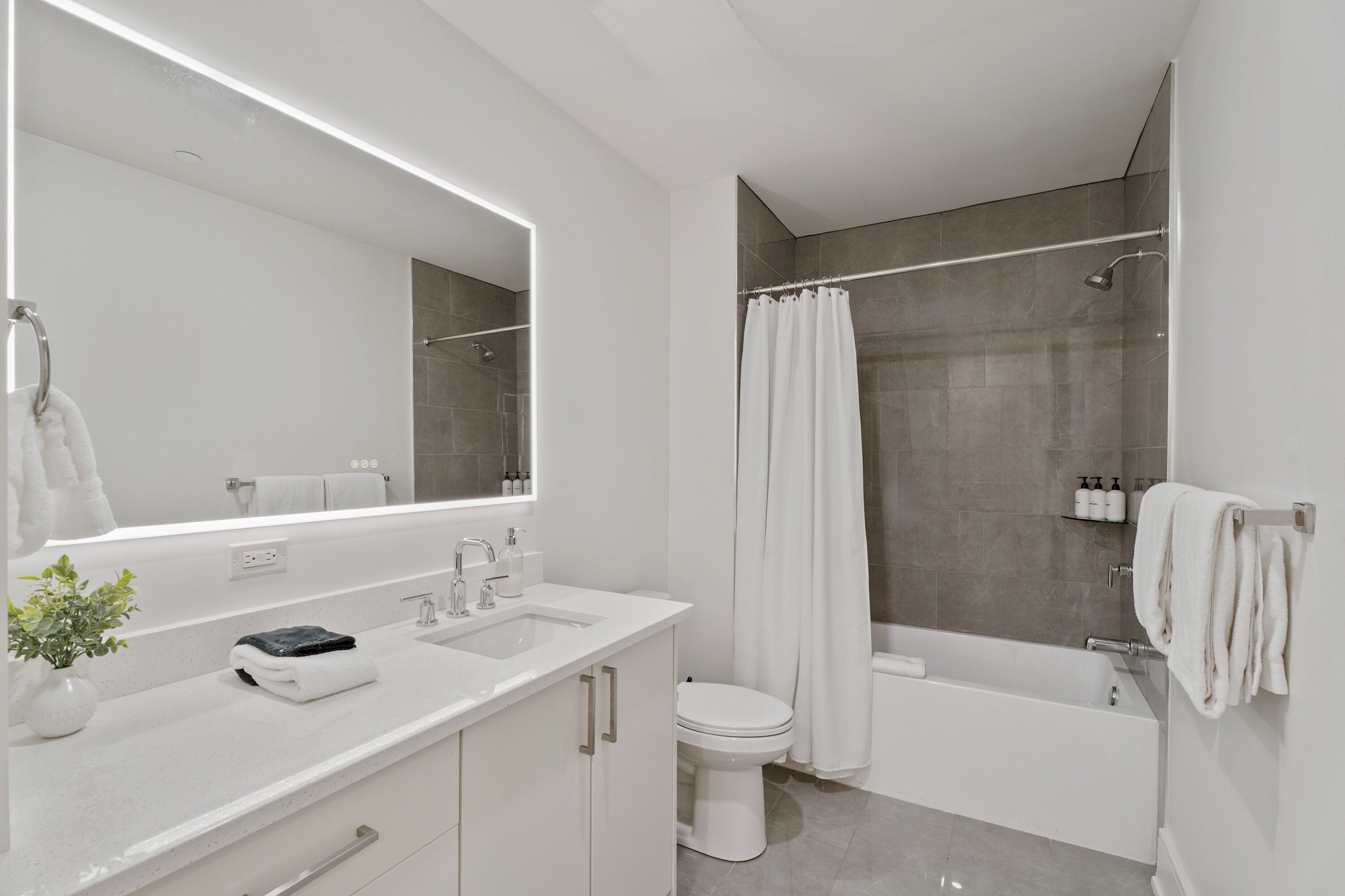 Un baño moderno con un espejo grande, dos lavamanos, un inodoro y una bañera.