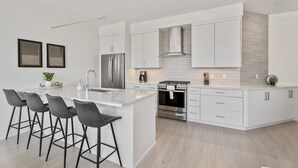 Una cocina moderna con armarios blancos, una isla central con taburetes de bar, electrodomésticos de acero inoxidable y piso de madera clara.