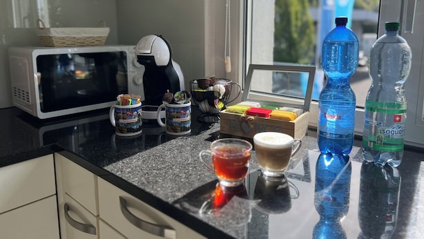 A kitchen counter with a coffee maker, mugs, a box of chocolates, and water bottles. - Very nice apartment in the heart of Interlaken with all amenities (Matten bei Interlaken)