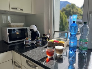 A kitchen counter with a coffee maker, mugs, a box of chocolates, and water bottles. - A beautiful apartment in the heart of Interlaken with all amenities   (Matten bei Interlaken)
