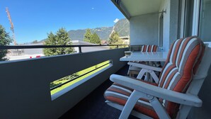A balcony with two striped chairs and a small table, overlooking a construction site and mountains. - Very nice apartment in the heart of Interlaken with all amenities (Matten bei Interlaken)