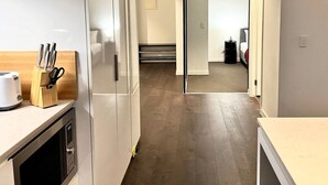 Una cocina moderna con microondas, tostadora y bloque de cuchillos. Una puerta corrediza da acceso a un dormitorio con cama y mesita de noche.