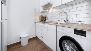 Una cocina compacta con armarios blancos, lavavajillas integrado y un fregadero con encimera de madera.