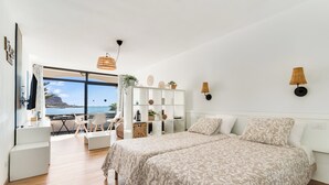 A modern bedroom with a large bed, a desk, and a view of the ocean. - Home2Book Cosy Studio, Pool & Sea Views Mogán (Mogán)