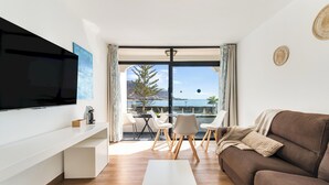 A modern living room with a flat-screen TV, a brown sofa, a white coffee table, and a dining area with chairs and a table. - Home2Book Cosy Studio, Pool & Sea Views Mogán (Mogán)