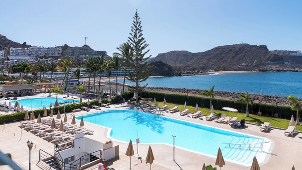 A pool area with lounge chairs and umbrellas, overlooking a beach and ocean. - Home2Book Cosy Studio, Pool & Sea Views Mogán (Mogán)