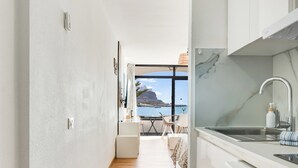 A modern kitchen with white cabinets, a marble countertop, and a view of the sea. - Home2Book Cosy Studio, Pool & Sea Views Mogán (Mogán)