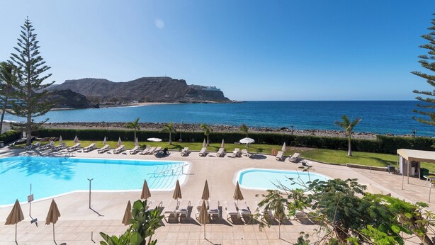 Une piscine d’hôtel avec des chaises longues et des parasols, offrant une vue sur une plage et l’océan.