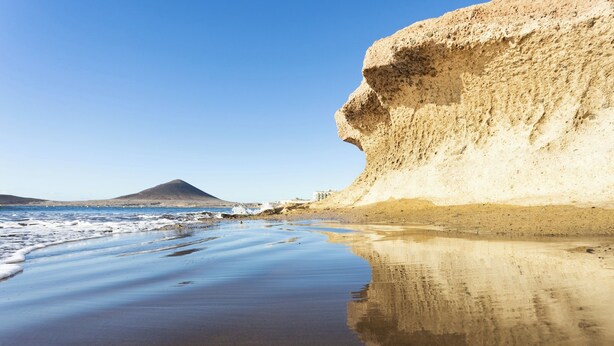 Una playa con arena y un acantilado grande.