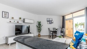 Una sala de estar moderna con televisor, comedor y ventanas amplias.