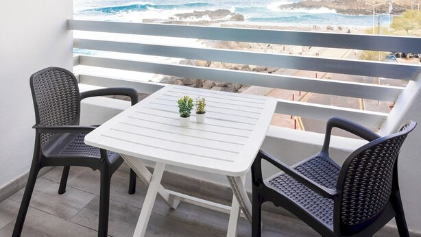 A balcony with a white table and two chairs, overlooking a rocky coastline and ocean. - Home2Book Ocean Breeze Terrace Stay, Mesa del Mar (Mesa del Mar)