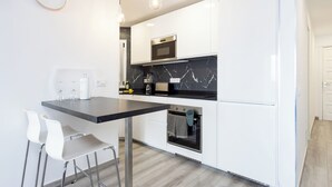 A modern kitchen with white cabinets, a black countertop, and stainless steel appliances. There is a dining area with white chairs and a small table. - Home2Book Ocean Breeze Terrace Stay, Mesa del Mar (Mesa del Mar)
