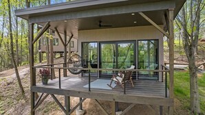 Una terraza moderna de madera con paredes de vidrio, ventilador de techo y mobiliario exterior.
