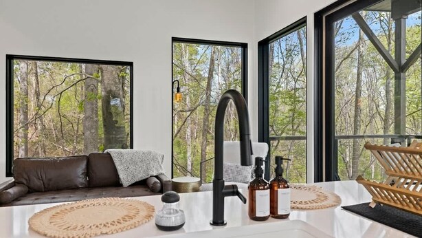 Un baño moderno con ventanas amplias, un grifo negro y un perchero de madera.