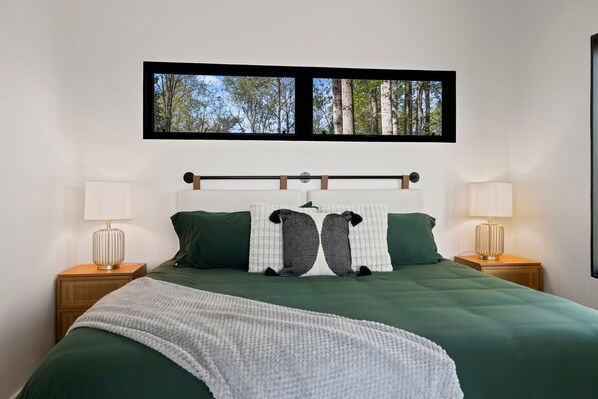 A bed with a view of trees through a window, two bedside lamps, and a headboard with a horizontal bar.