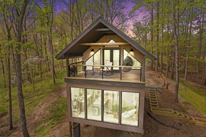 A modern treehouse with a balcony, large windows, and a wooden deck.