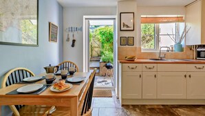 A modern kitchen with a dining area, featuring a wooden table, chairs, and a view of the garden through the open door.