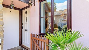 A building entrance with a wooden gate, a door with a number plate, and a potted plant.