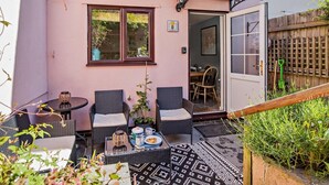 An outdoor patio with wicker furniture, a small table with a teapot and cups, and a patterned rug.
